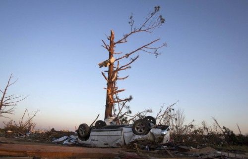 An upturned truck lies under tree that has lost most of its branches, following tornado near Vilonia, Arkansas, at sunset