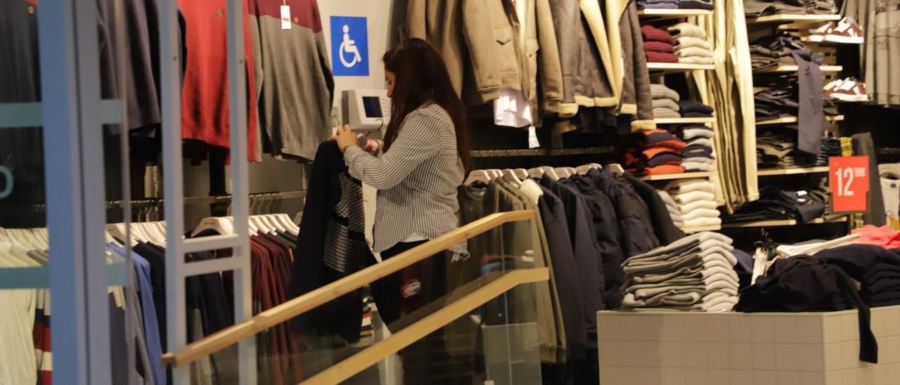 Una trabajadora de una tienda del centro de Gandia cuelga una prenda de ropa de la exposición. | XIMO FERRI