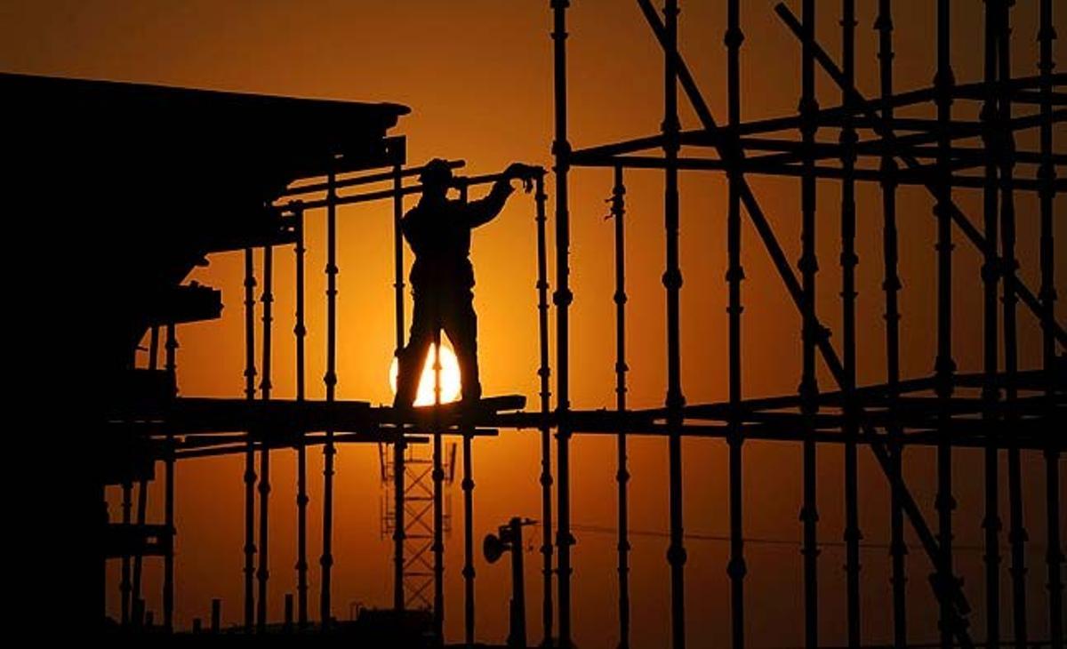 Es fa de dia mentre un treballador instal·la una bastida en una obra de construcció del tren d’alta velocitat al viaducte de Hefei (Xina).