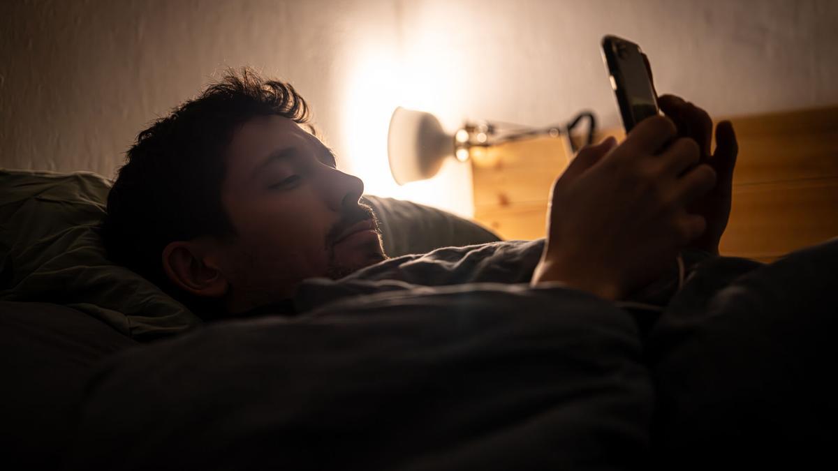 Un hombre descansa en la cama mientras utiliza su teléfono móvil.