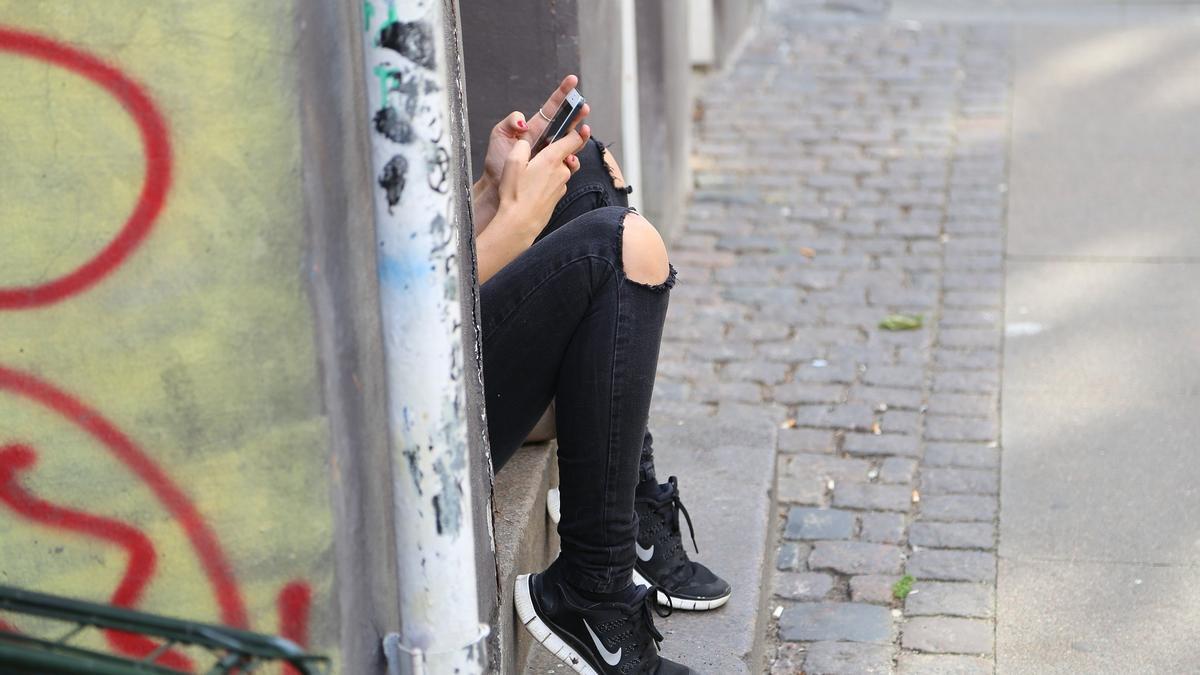 Archivo - Imagen de archivo de una adolescente con un móvil en la calle.