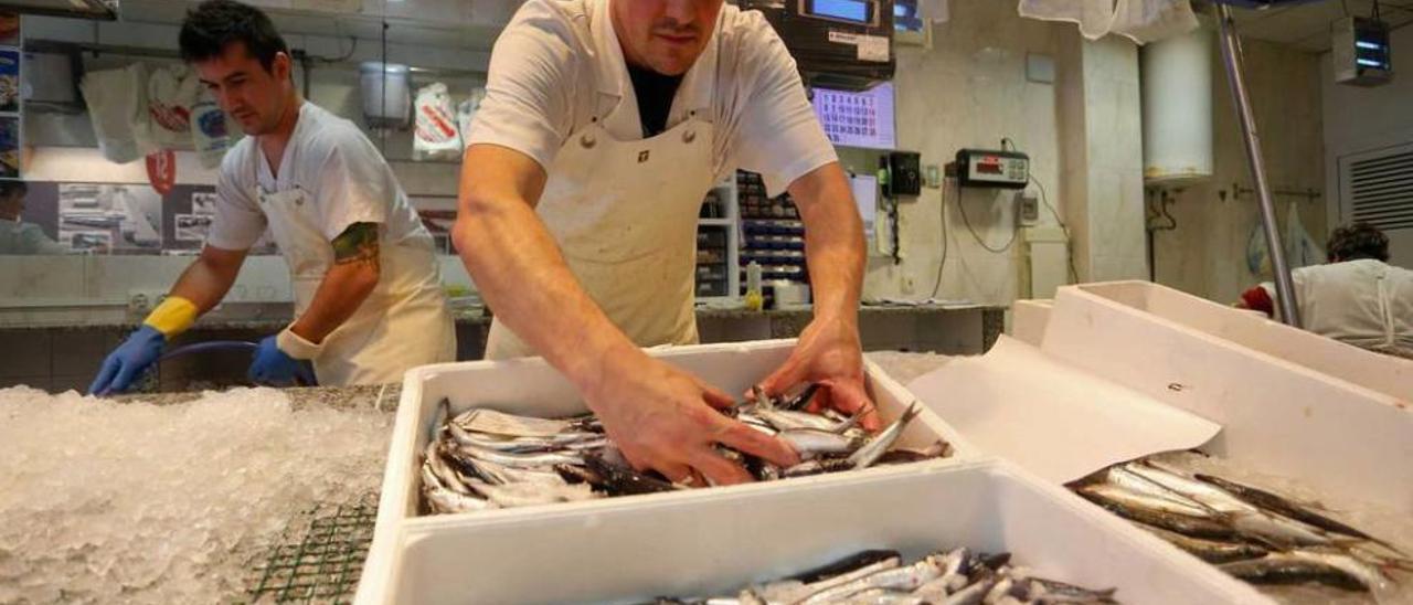 Samuel Guillén repone bocarte en el mostrador de su pescadería mientras Javier Serrano limpia el suelo.