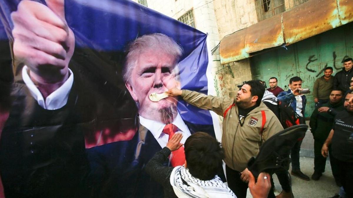 Manifestantes palestinos golpean con zapatos un póster con la imagen de Trump durante una protesta en Hebrón (Cisjordania), el 24 de febrero.