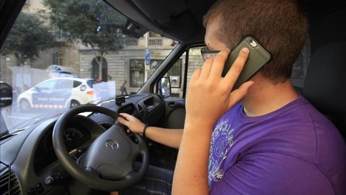 Un conductor habla por el móvil mientras espera el verde del semáforo, en Barcelona.