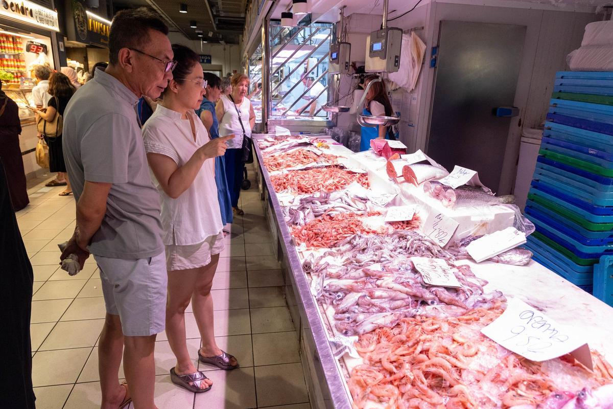 Unos clientes observan el pescado de uno de los puesto del Mercado.