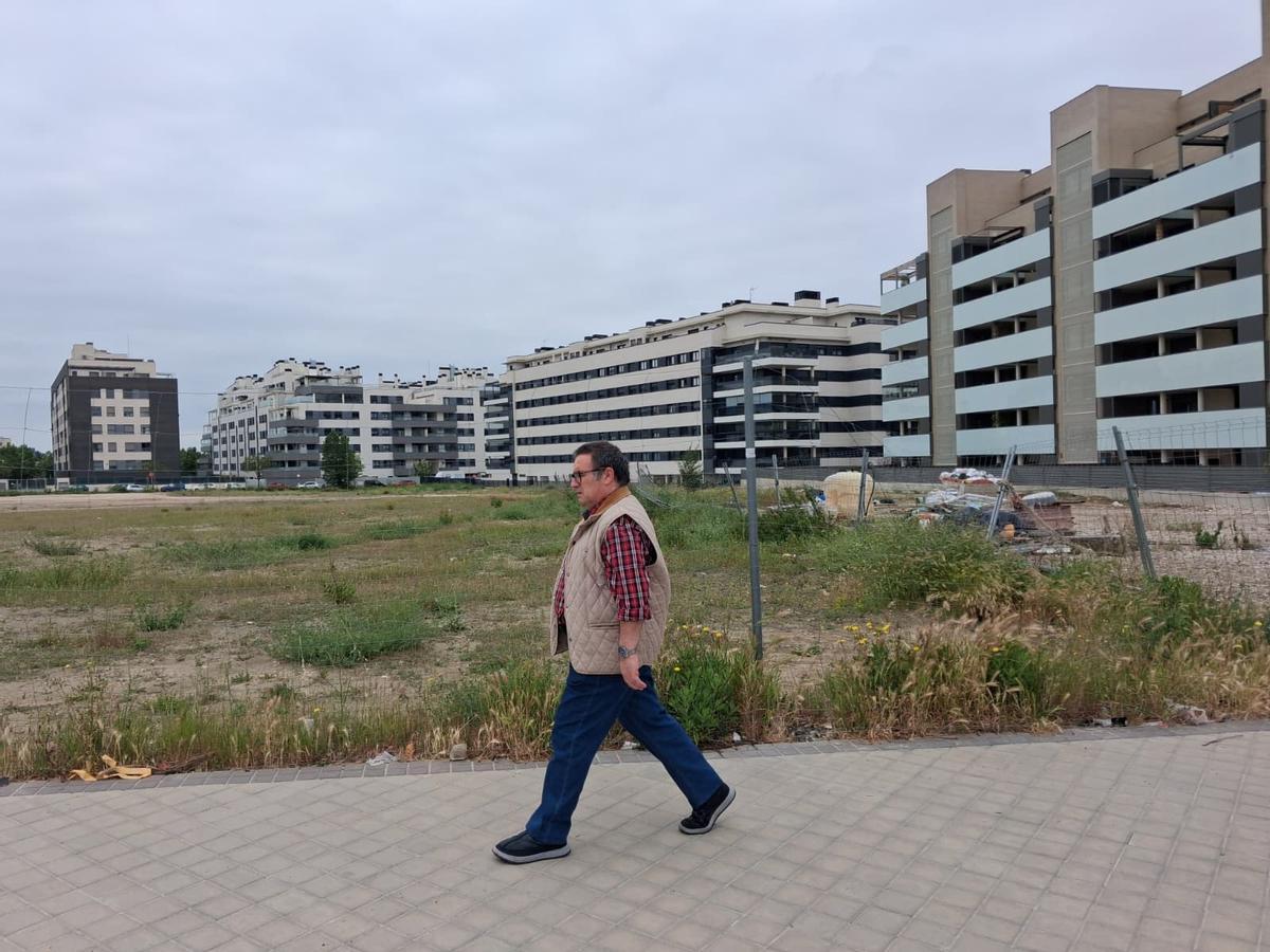 Un hombre pasea frente a un solar vacío y un bloque de viviendas al lado en el nuevo desarrollo del barrio de la Luna de Rivas-