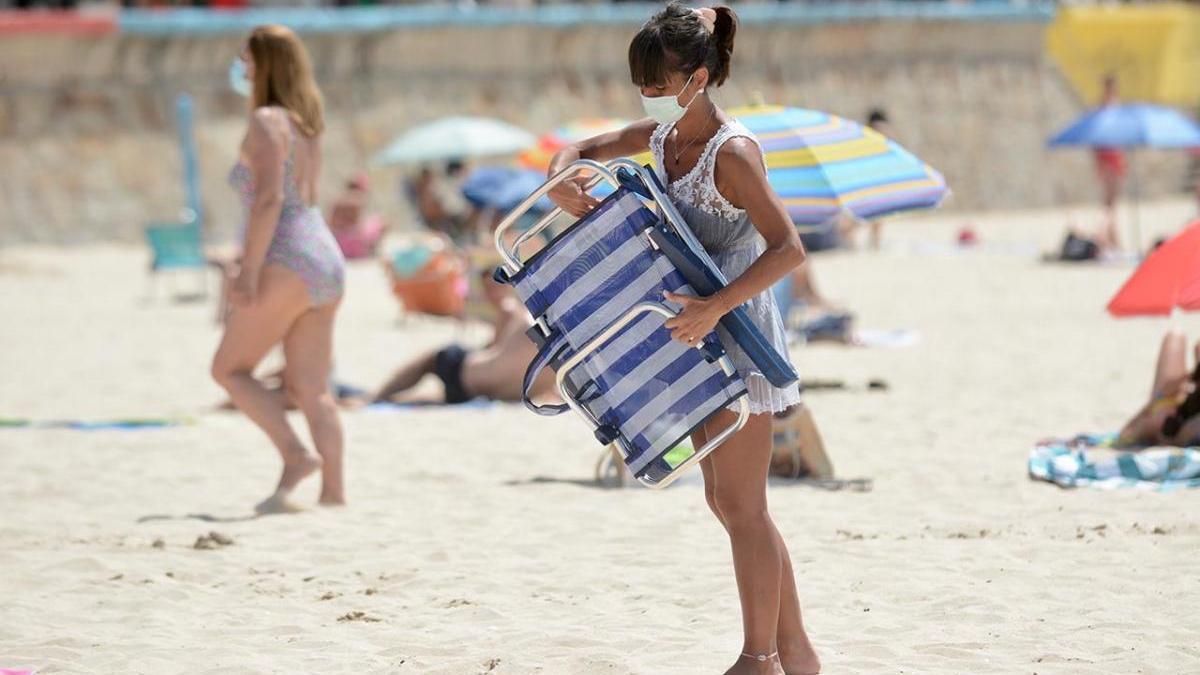 Una mujer con mascarilla llega a la playa de Silgar, en Sanxenxo