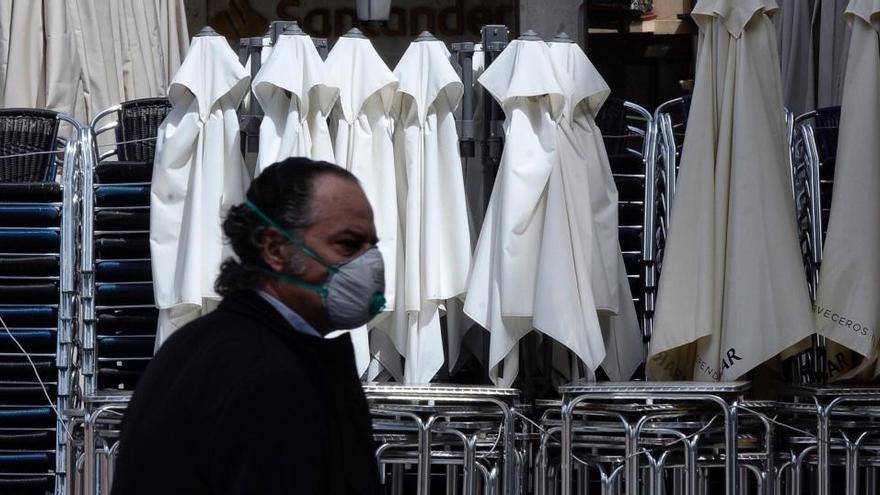 Un hombre ataviado con una mascarilla pasa por delante de una terraza