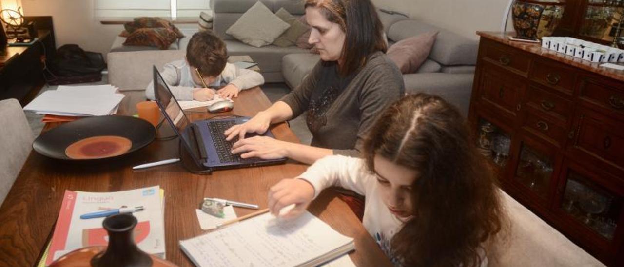 Una mujer teletrabaja mientras sus hijos hacen los deberes.