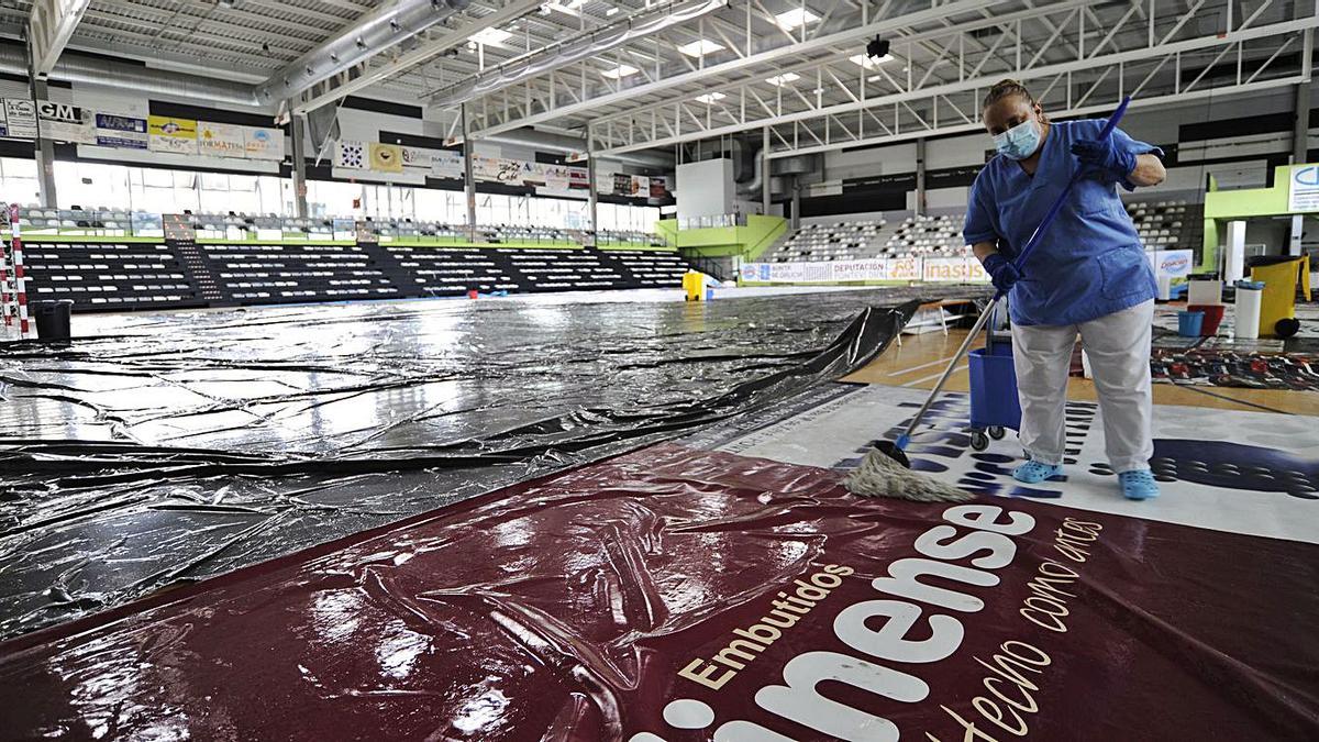 Una mujer pasa la fregona, ayer, sobre la lona que cubría la pista del Lalín Arena. |  // BERNABÉ/JAVIER LALÍN