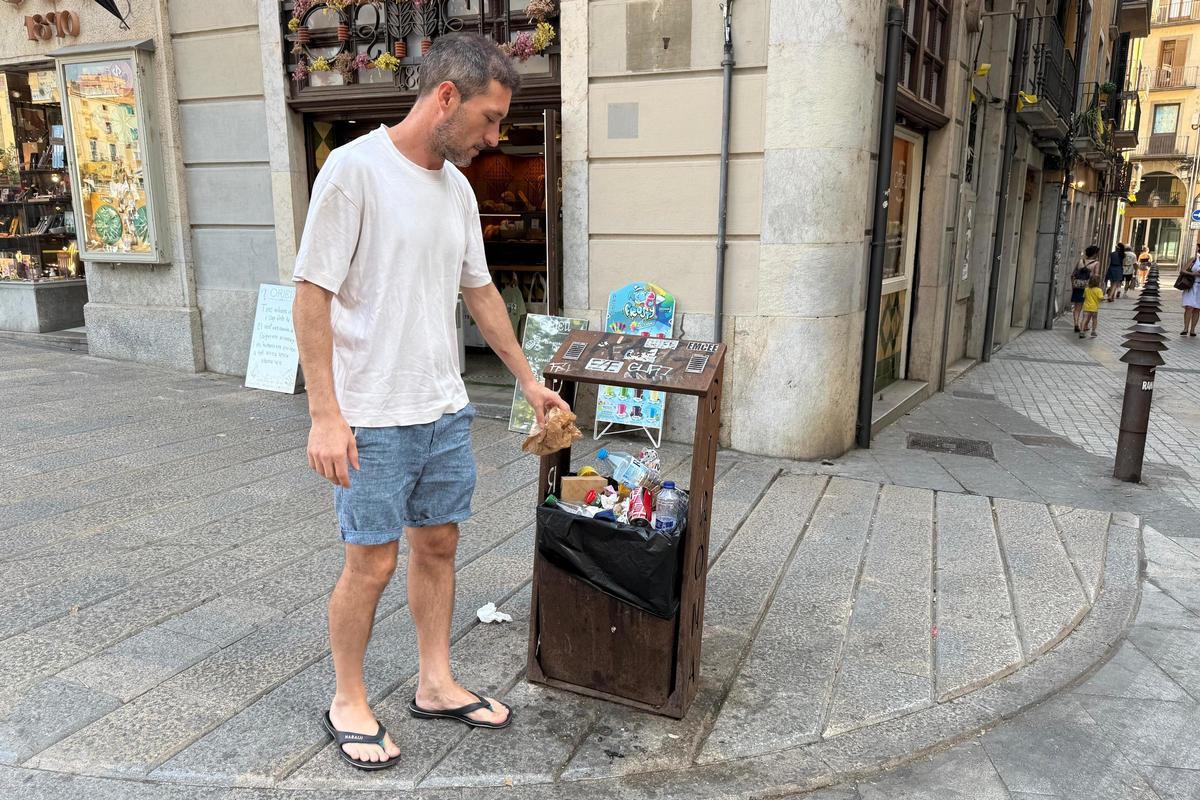 Un home tira un embolcall a una paperera a tocar del pont de Pedra de Girona.