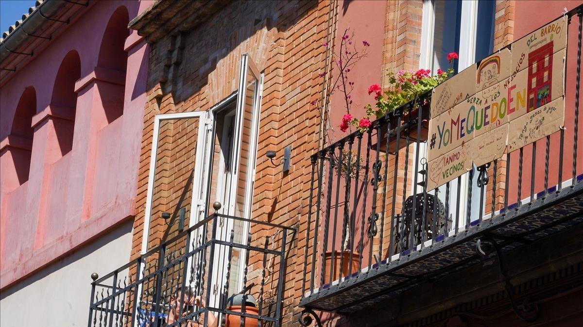 Flores en un balcón junto a una pancarta invitando a quedarse en casa, en un edificio de Sevilla.