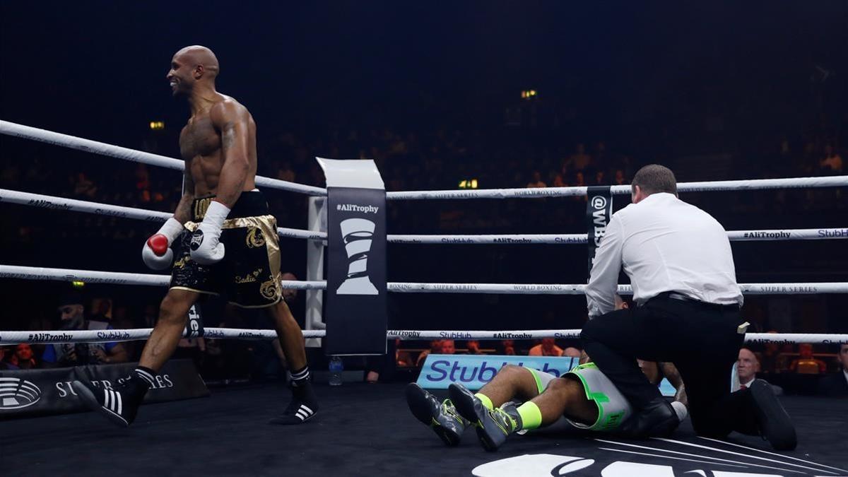 El boxeador Louis Adolphe da vueltas por el ring tras noquear a traición a Nathan McIntosh, atendido por el árbitro en la lona.