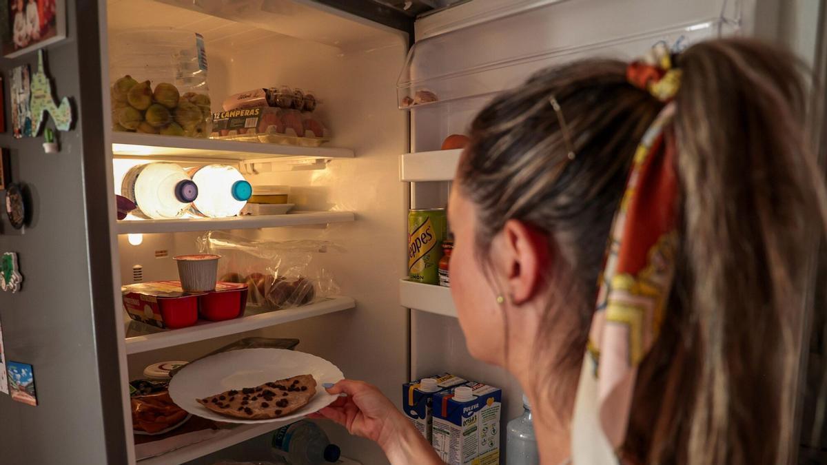 Una mujer, frente a la nevera de su cocina, llena de comida.