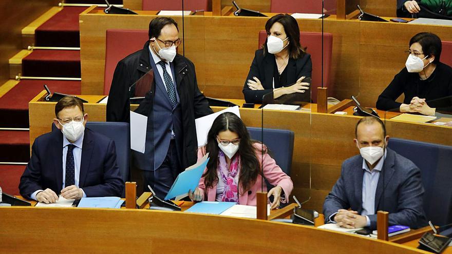 El conseller Soler pasa por detrás de Puig, Oltra y Dalmau, ayer durante el pleno de las Corts. | M.A.MONTESINOS