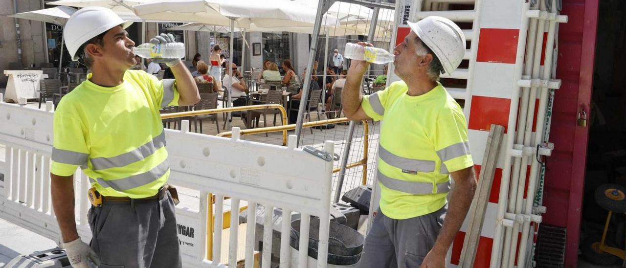 Dos obreros que participan en la reforma de Porta do Sol, ayer, bebiendo agua fría.