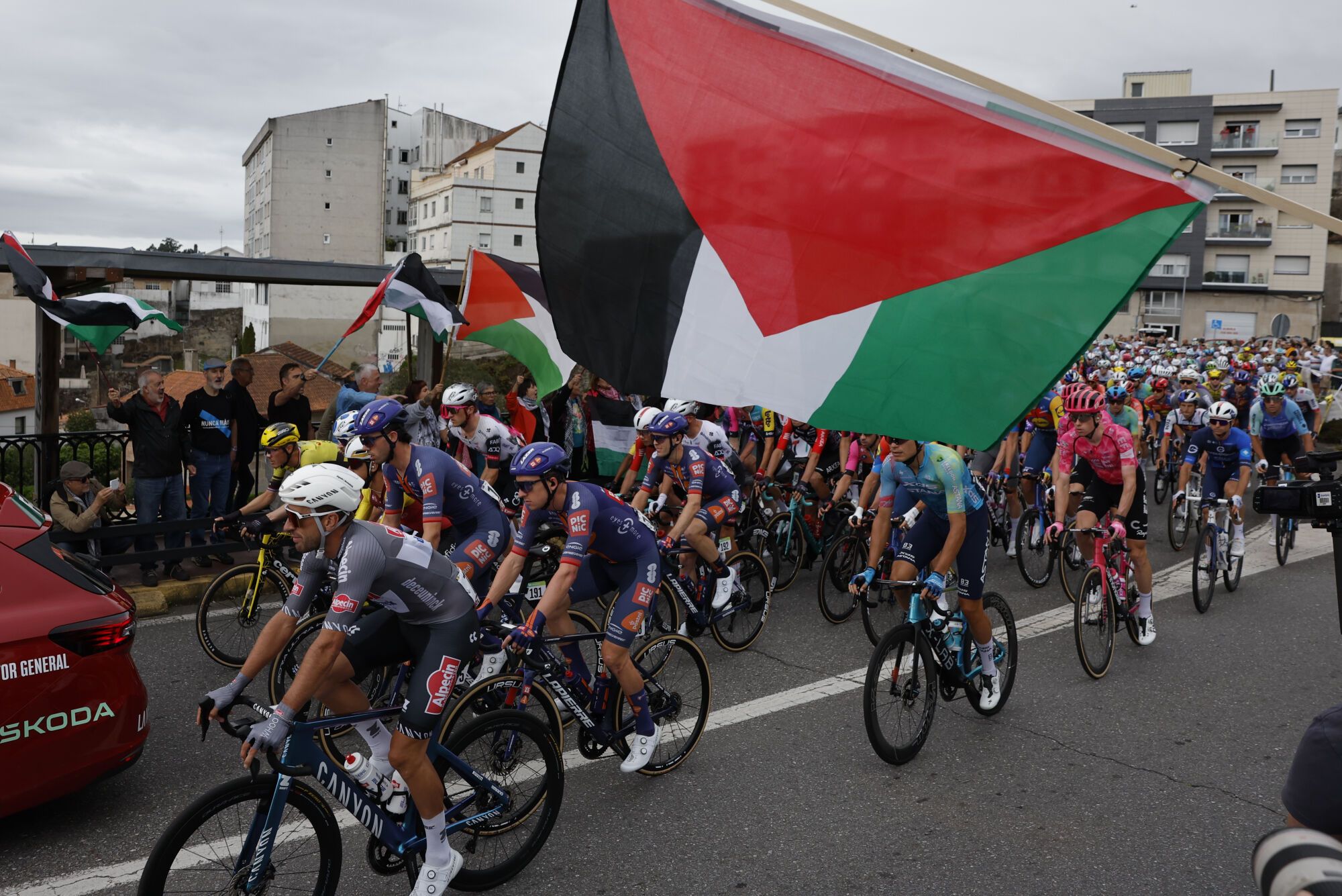 POIO (PONTEVEDRA), 09/09/2025.-El pelotón pasa ante la protetas propalestina durante la etapa 16 de la Vuelta Ciclista a España que se disputa este martes entre Poio y Mos-Castro de Herville (Pontevedra), de 167.9 km de recorrido. EFE/Lavandeira