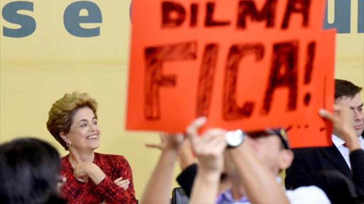 Rousseff sonríe ayer en un acto en Brasilia, mientras un asistente sostiene un cartel que dice «Dilma se queda».