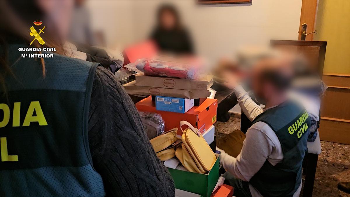 Agentes de la Guardia Civil inspeccionan las cajas halladas en casa de la detenida, sentada, al fondo de la imagen.