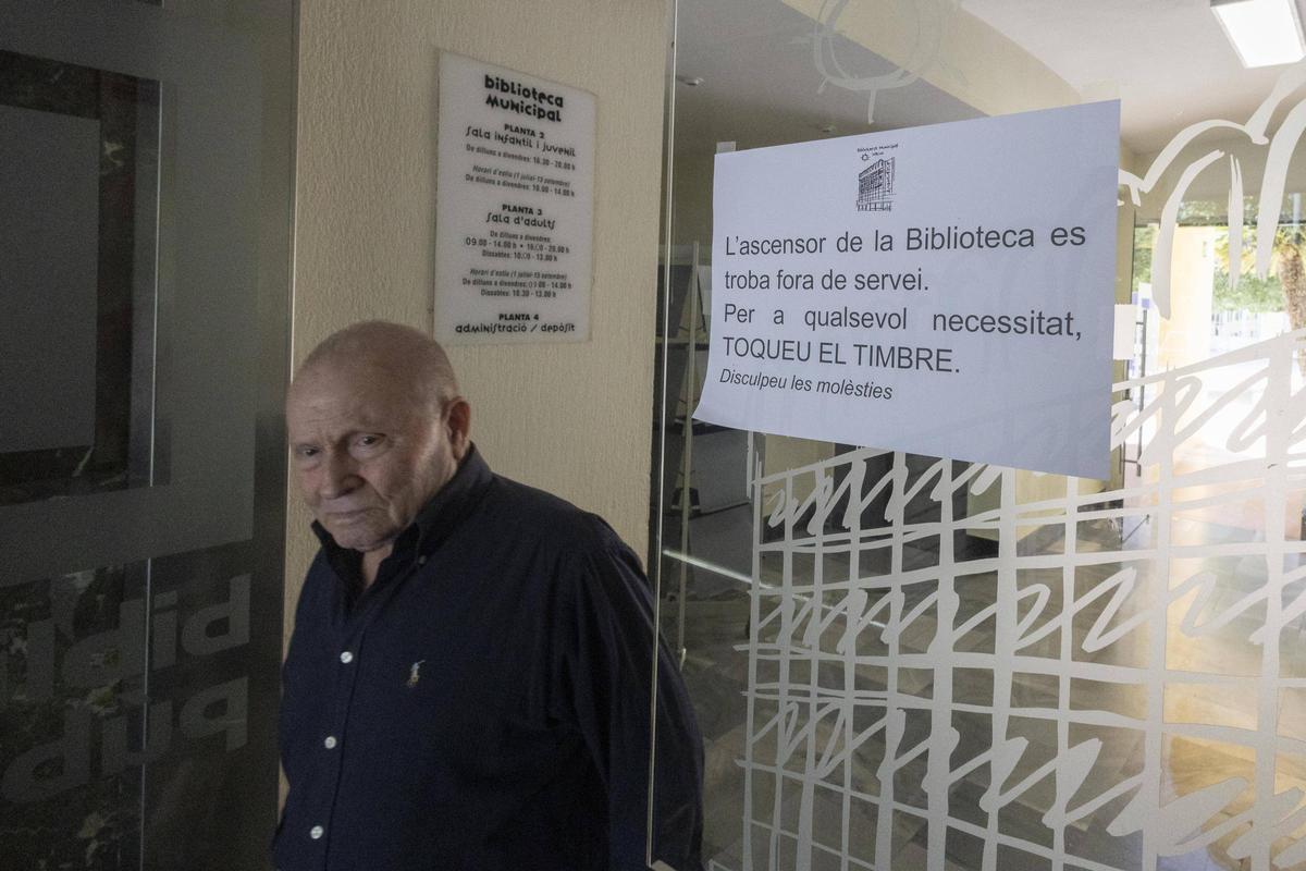 Un hombre cruza la puerta de acceso al patio de la biblioteca de Xàtiva, donde hay un cartel sobre el ascensor.