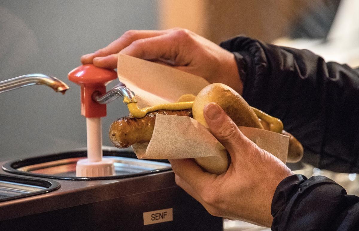 Ein Mann pumpt Senf auf eine Bratwurst im Brötchen.
