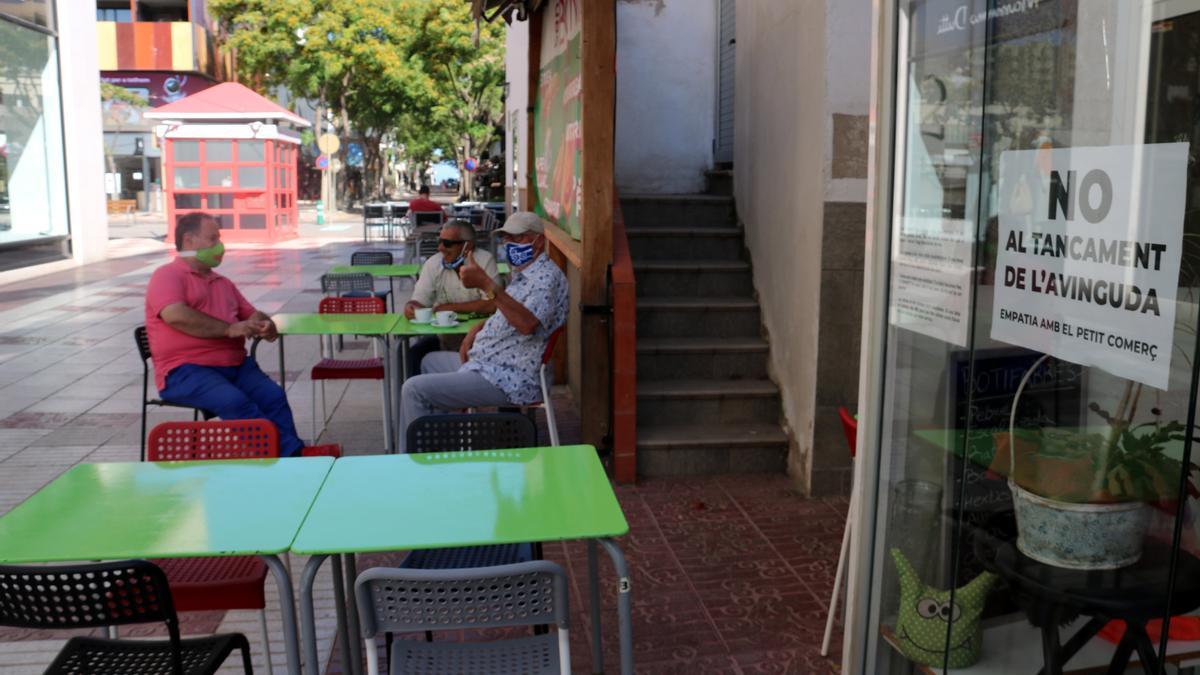 En primer terme un cartell contra el tall de l&#039;avinguda de Platja d&#039;Aro i, al fons, clients d&#039;un bar de les galeries. Foto publicada el 22 de juny del 2021 (horitzontal)