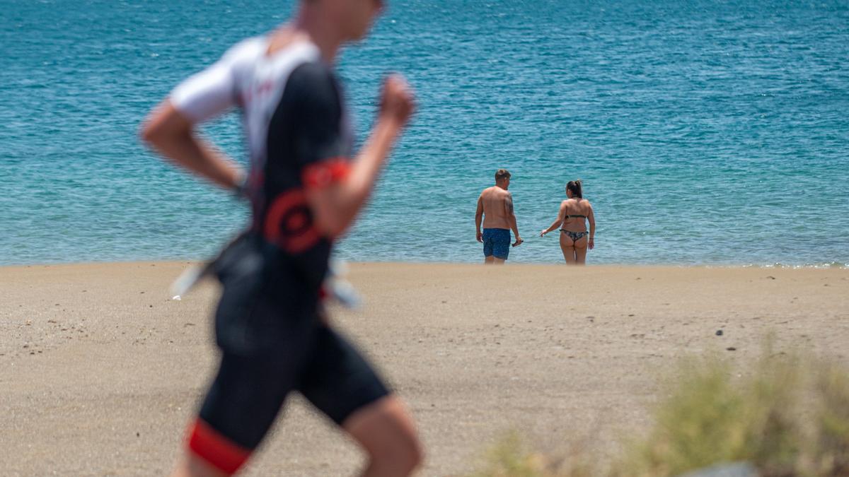 Corredor del Ironman este sábado en Puerto del Carmen (Lanzarote) y, al fondo, dos bañistas se disponen a meterse en el agua.