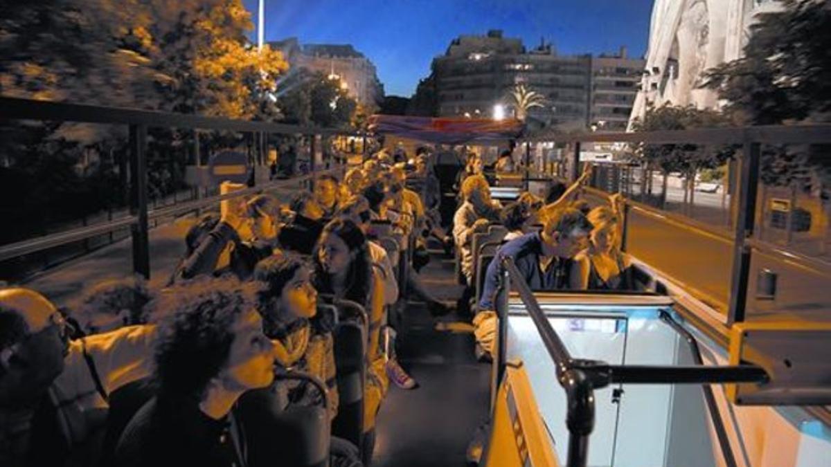 Visitantes en la planta superior de un bus turístico, en ruta por la ciudad y a su paso por la Sagrada Família.