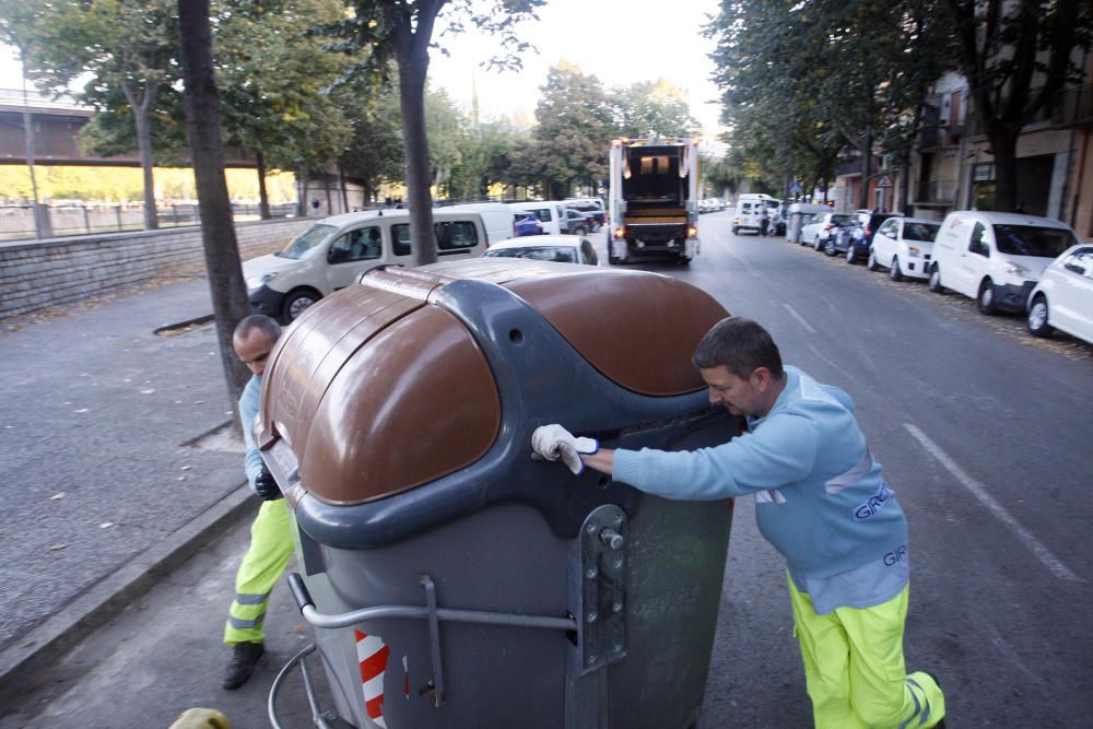 Carrers amb restes de mobiliari urbà cremat, contenidors per terra i treballadors de la brigada treballant