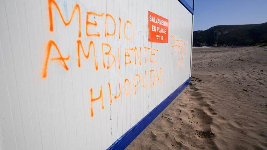 La caseta de salvamento de Bayas, con pintadas. A la derecha, jóvenes ayer en el playón.