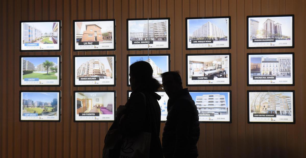 Dos personas pasan por el escaparate de una inmobiliaria.