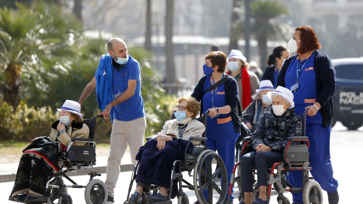 Personas mayores en silla de ruedas llevados por sus cuidadores por la plaza del Ayuntamiento