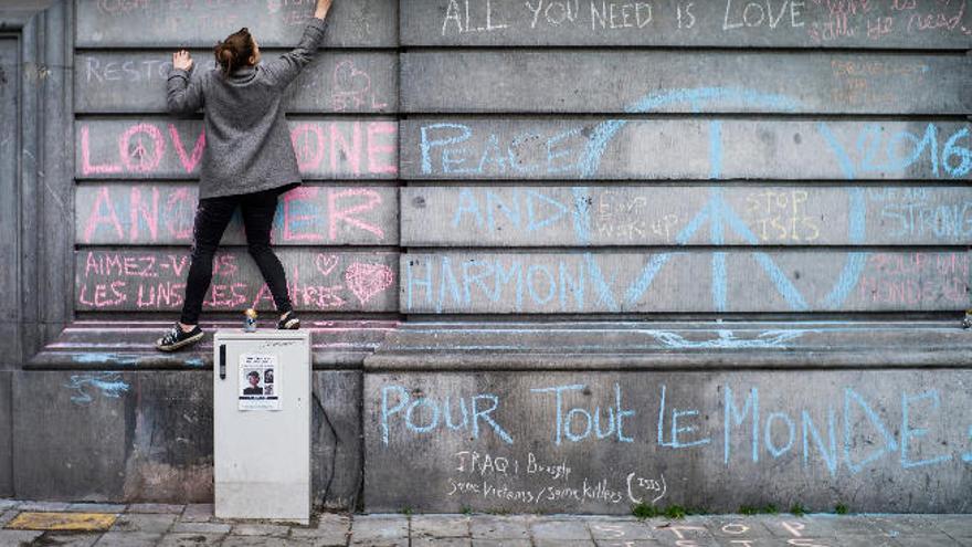 Una chica escribe un mensaje en recuerdo de las víctimas del atentado del martes pasado en un muro de la Plaza de la Bolsa de Bruselas (Bélgica), un día después de los atentados.