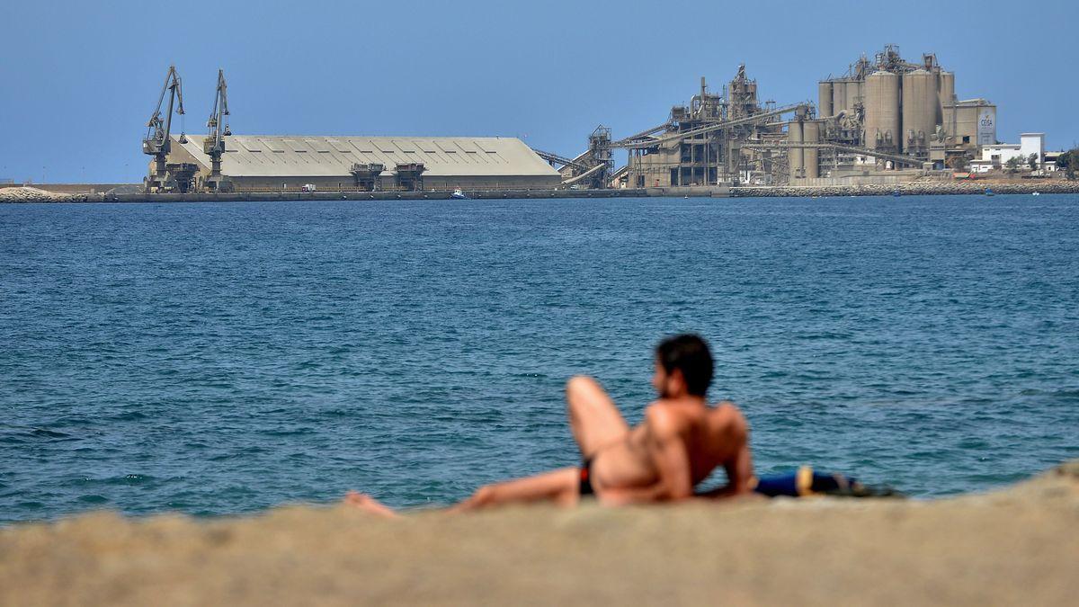 Un bañista toma el sol frente a la fábrica de cemento del muelle de Santa Águeda.