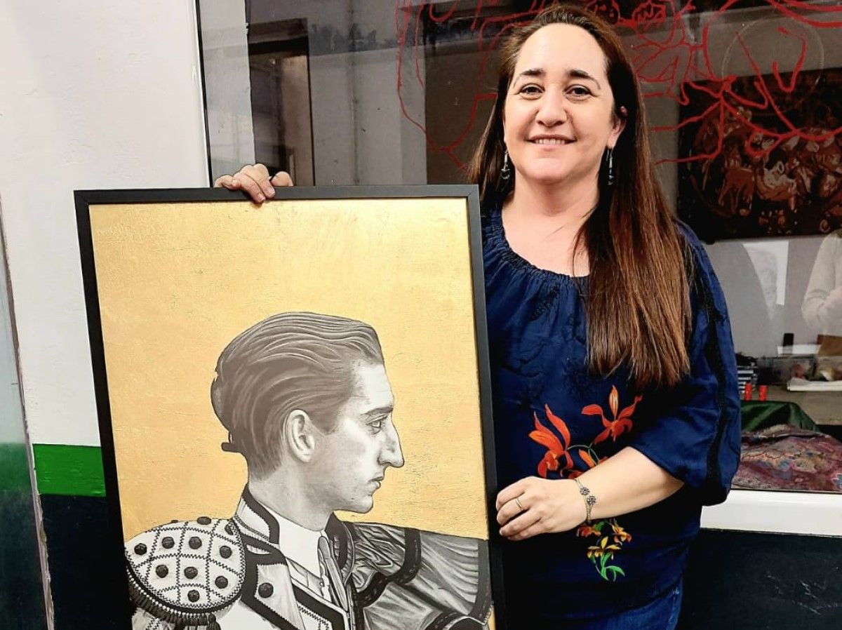 Mercedes Fidalgo Domínguez posando con el retrato de Manolete, cartel de la reciente Feria de la Comunida de Madrid.