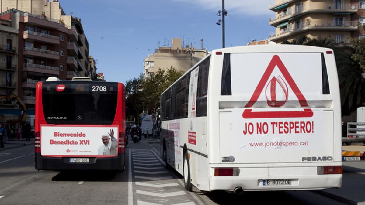 El autobús organizado por asociaciones laicas y ateas, a la derecha, junto a un autobús con una publicidad que da la bienvenida al Papa, hoy, en la calle Marina, delante de la Sagrada Família.