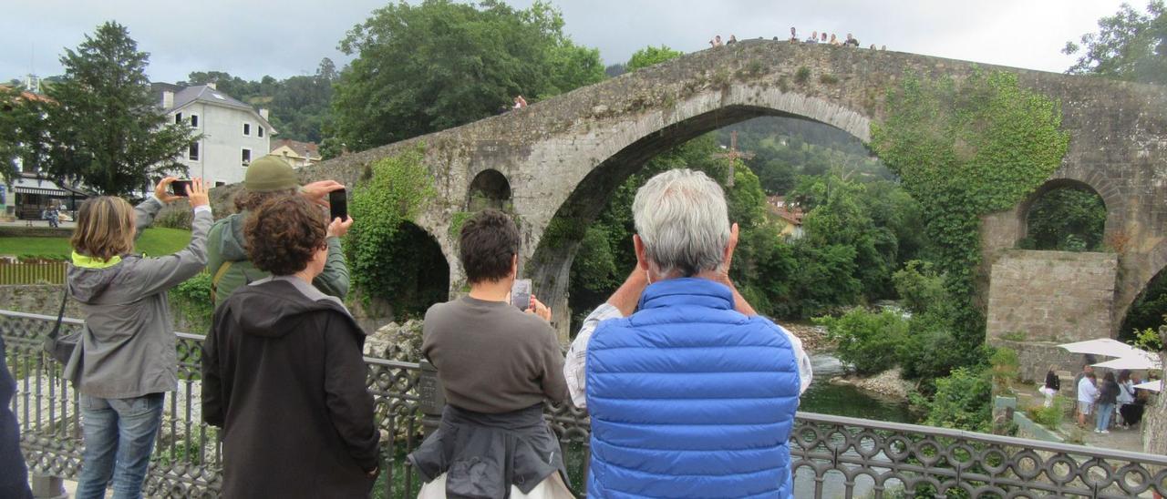 Varios turistas, ayer, en Cangas de Onís, haciendo fotos con el móvil al emblemático puente «romano». | J. M. Carbajal