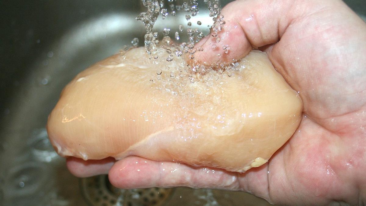 Una persona lava un trozo de pollo con agua