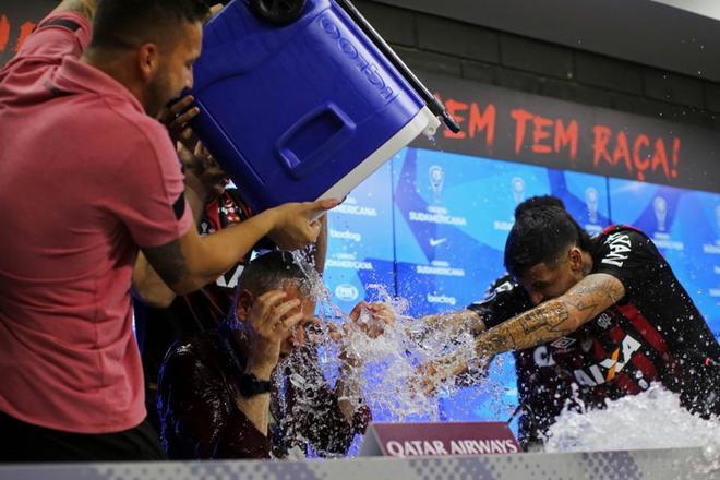 Tiago Nunes (C), recibe agua de Luis González (R) y otros jugadores durante la conferencia de prensa tras ganar el partido de fútbol de la segunda ronda de la Copa Sudamericana de 2018 contra Colombia Junior en el estadio Arena da Baixada en Curitiba