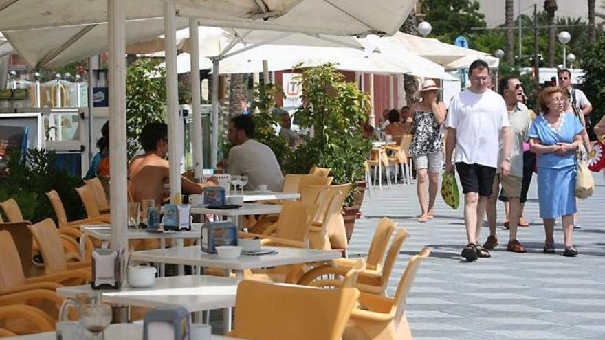 Turistas caminando junto a unas de las terrazas del paseo de Gómiz en la playa del Postiguet.