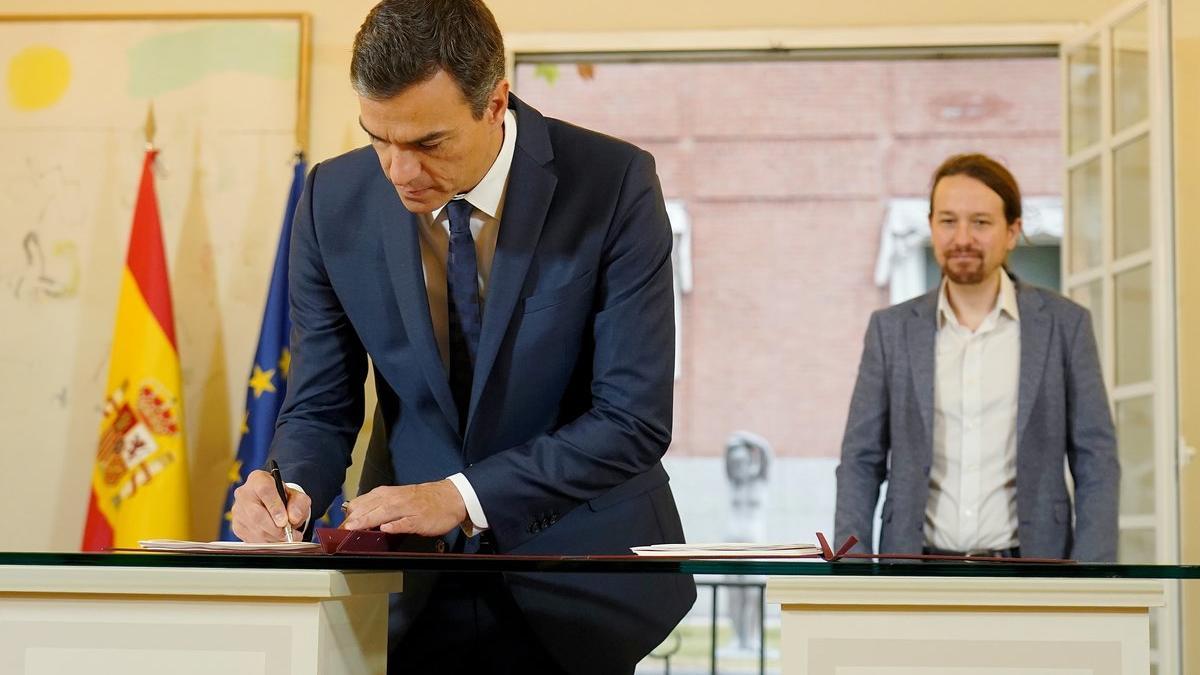 El presidente del Gobierno, Pedro Sánchez, firma el acuerdo presupuestario ante la mirada del líder de Podemos, Pablo Iglesias, este jueves en la Moncloa.