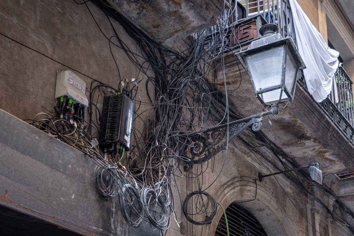 Imágenes de cableado eléctrico enmarañado en fachadas, bajantes y otros elementos de edificios, visibles desde la calle