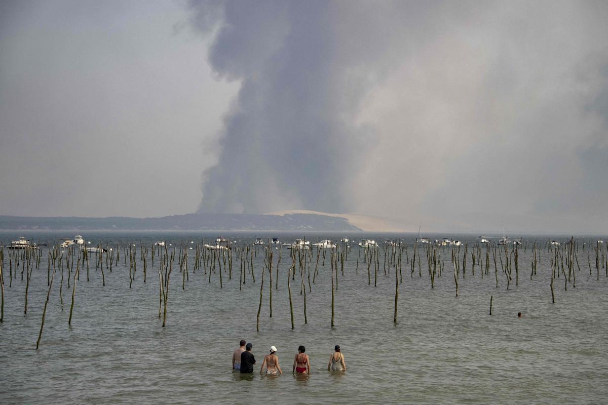 Turistas observan la oscura columna de humo sobre la Dune de Pilat, desde Cap Ferret, originada por un incendio forestal cerca de La Teste, al sur de Francia, el 18 de julio del 2022.