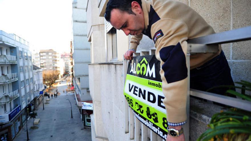 Una persona coloca el cartel de venta de vivienda // l. Abella