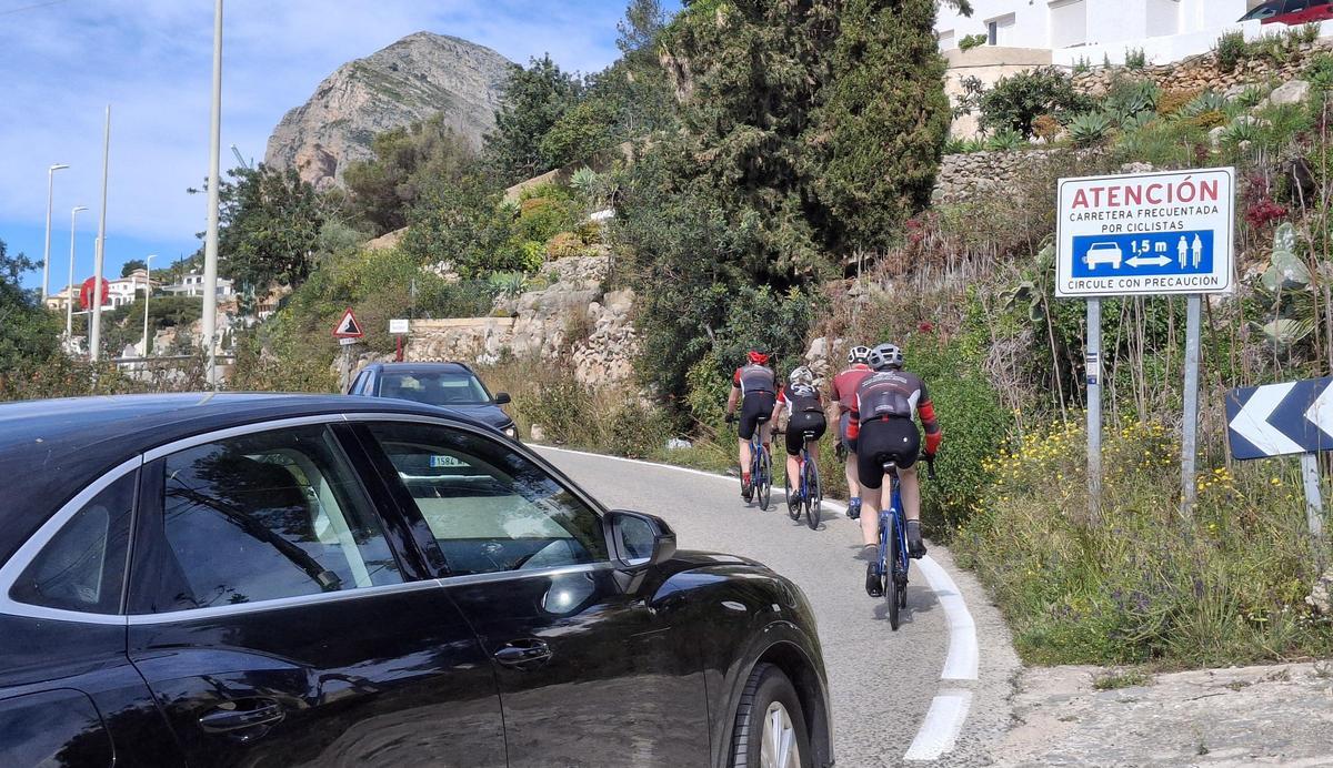 Ciclistas ascienden les Planes y pasan junto a un cartel que recuerda la distancia al adelantar