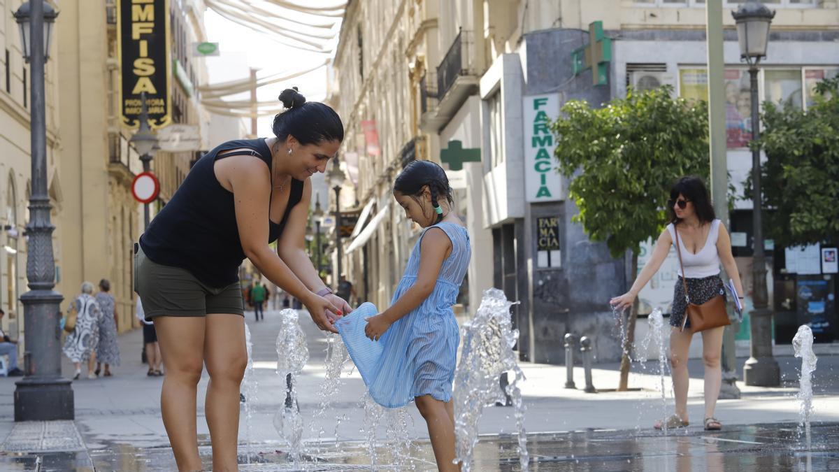 Una niña se refresca con su madre en la fuente de Las Tendillas.