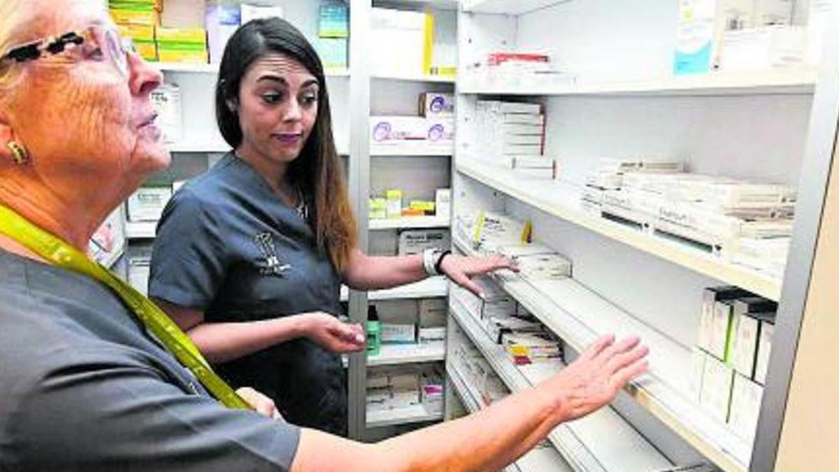 Dos trabajadoras buscan un medicamento en los estantes en una farmacia.