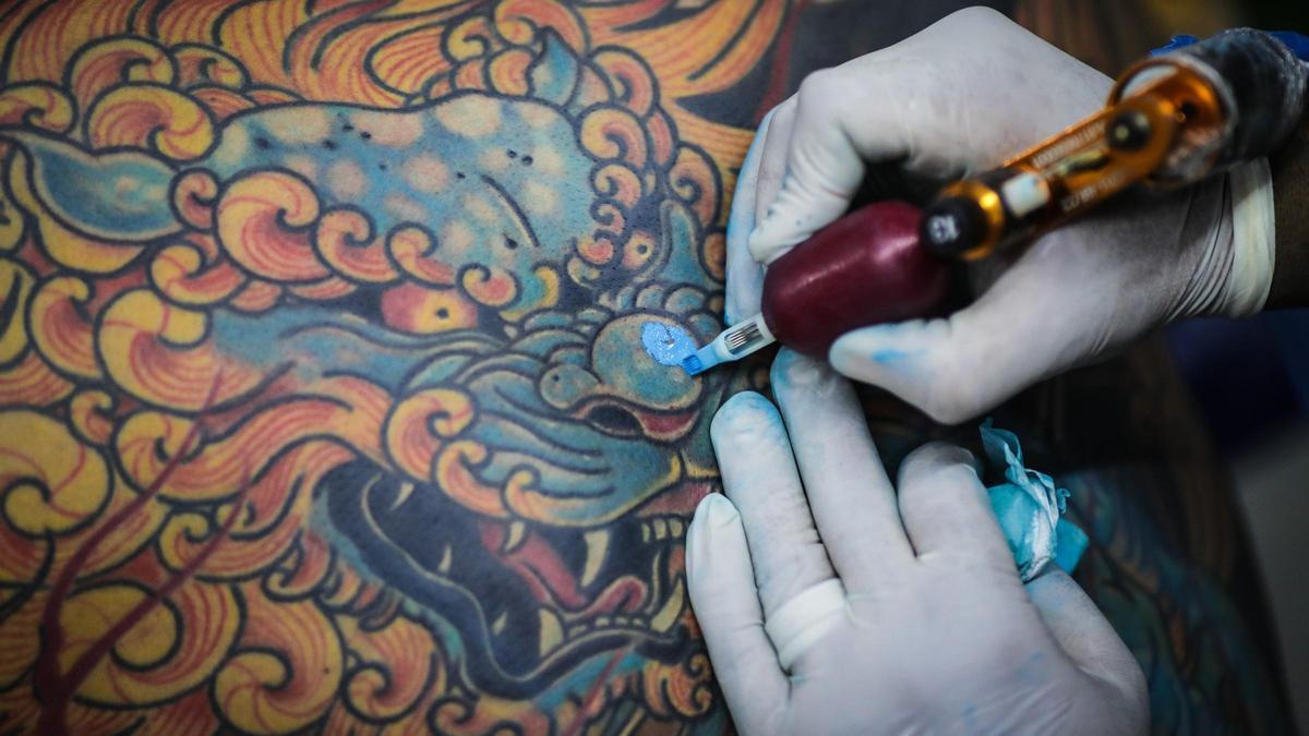 Un tatuador utiliza tinta azul mientras realiza uno de sus diseños