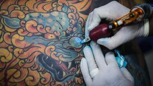 Un tatuador utiliza tinta azul mientras realiza uno de sus diseños.