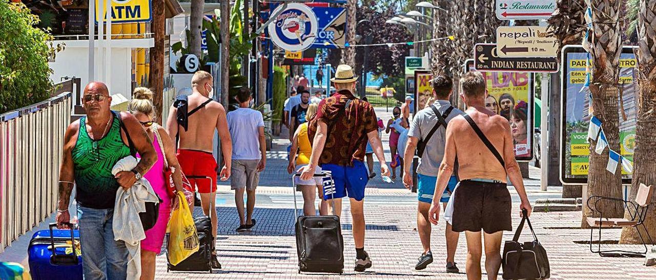 Turistas cargados de maletas caminan ayer por una calle de Benidorm, donde muchos hoteles siguen cerrados. DAVID REVENGA